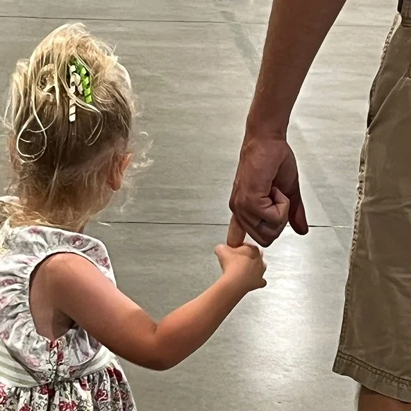 Young girl holds onto a parent's finger as they walk together at church.