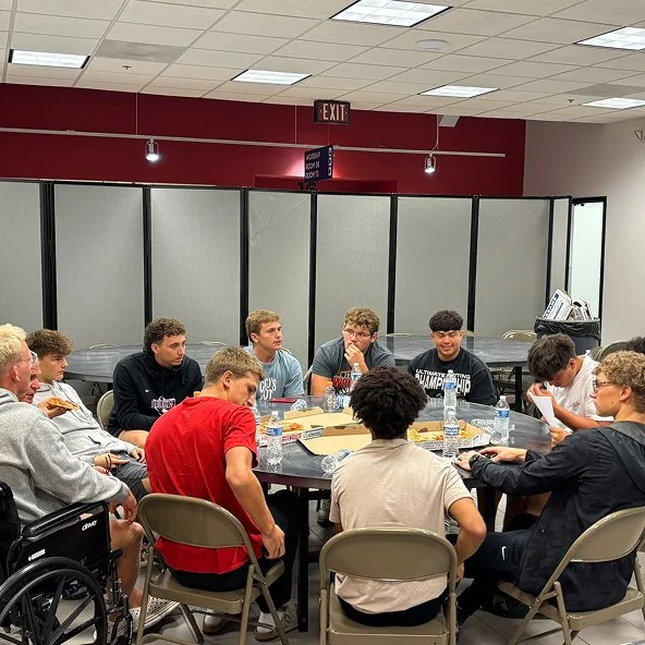 Young men gather around a table with pizza during a small group meeting.