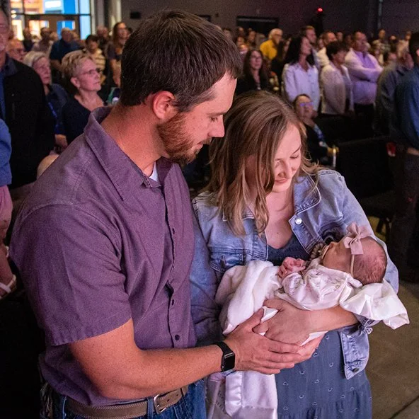 Parents hold their infant before the congregation during a baptism service.