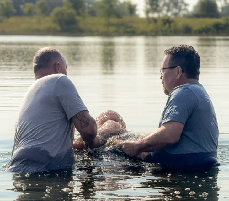 Two men in the river baptising another men.
