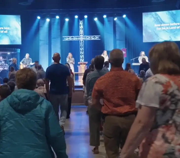 Congregation stands during a contemporary worship service as the band leads with lyrics on screens.