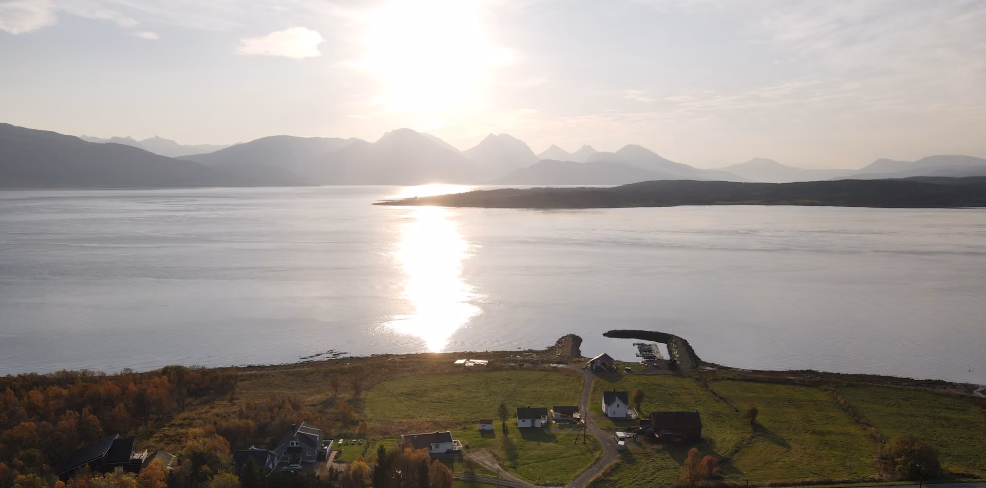 Sunset over calm water with distant mountains and a small coastal village in the foreground.
