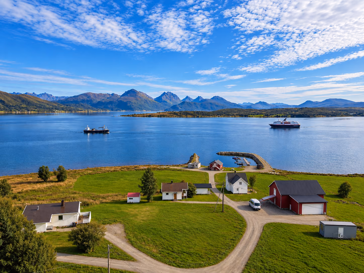 Aerial view of Larseng Kystferie by the sea on Kvaløya, with waterfront accommodation, a small harbour, fjord and surrounding mountains.