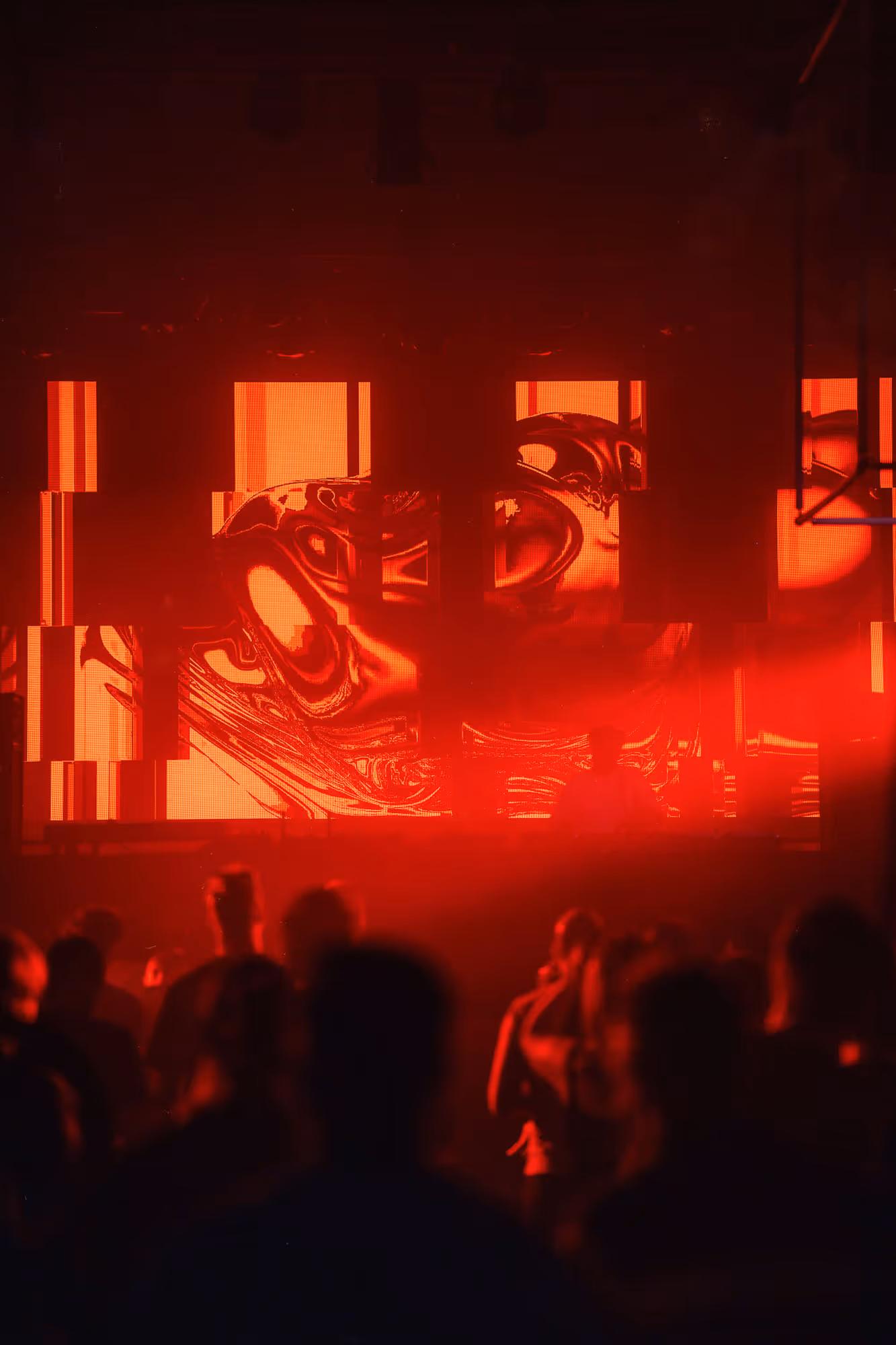 Silhouettes of people in a dark club with a DJ and vibrant red abstract visuals on screens behind.