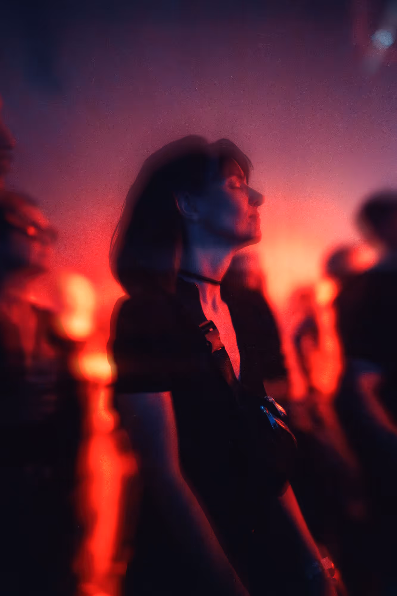 Woman with closed eyes bathed in red light at a crowded event with blurred figures around her.