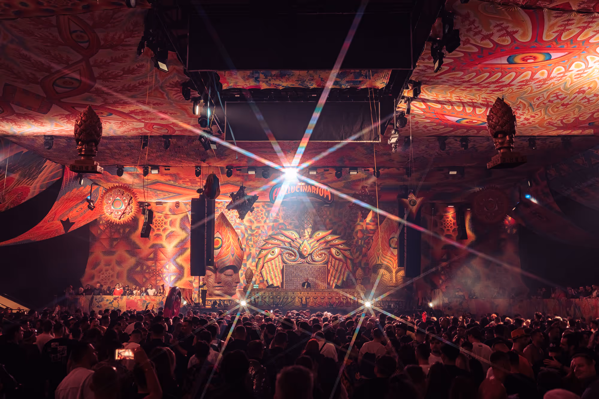 Crowded psychedelic-themed nightclub with colorful lights and a DJ booth labeled Hallucinarium.