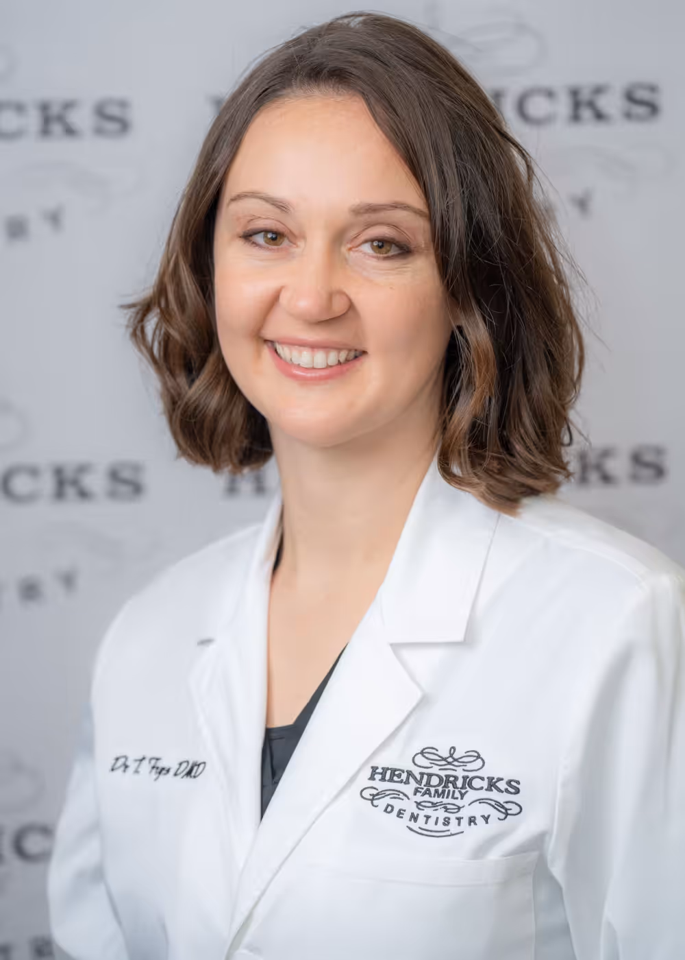 Smiling woman with brown hair wearing a white Hendricks Family Dentistry coat.