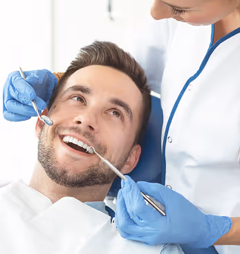 Dentist examining smiling man's teeth with dental tools in a clinic.