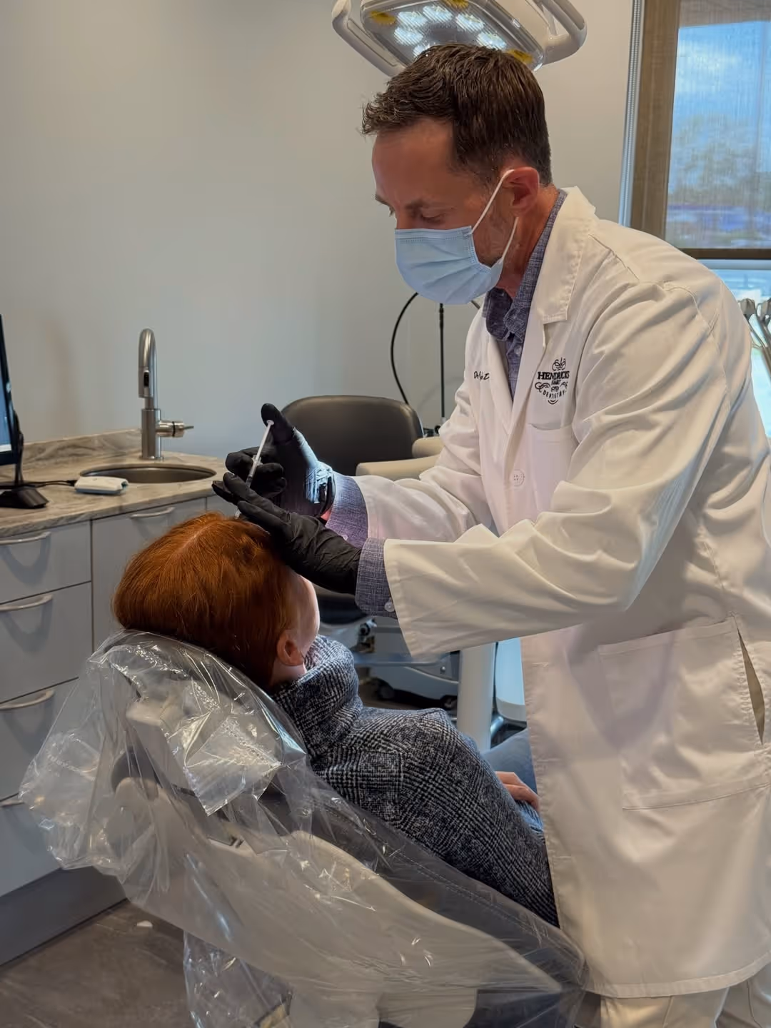 Doctor in lab coat and mask preparing to inject a patient's scalp in a medical office.