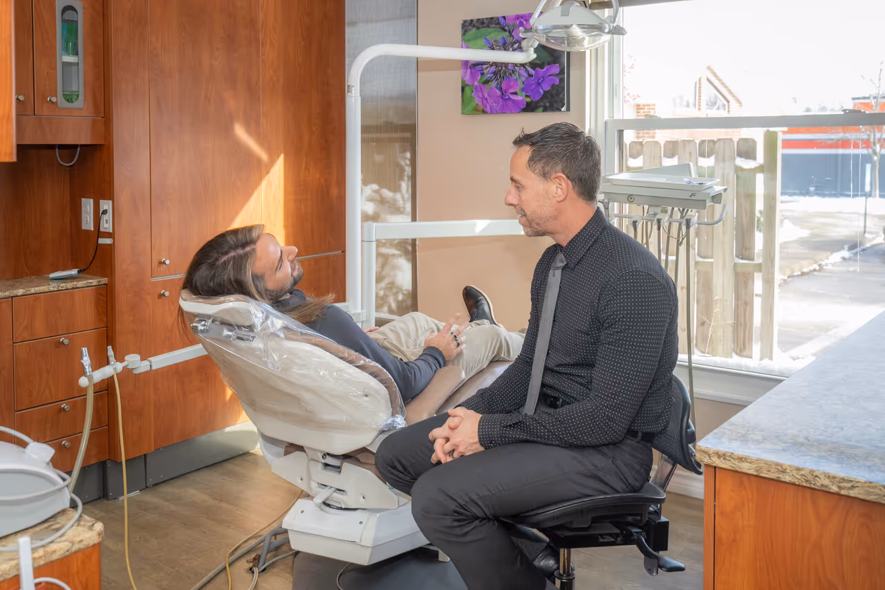 Dentist talking to relaxed male patient in chair at a bright dental office.
