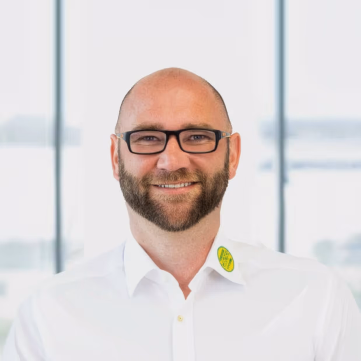 Mann mit Brille und Bart lächelt, trägt weißes Hemd mit ESG-Logo
