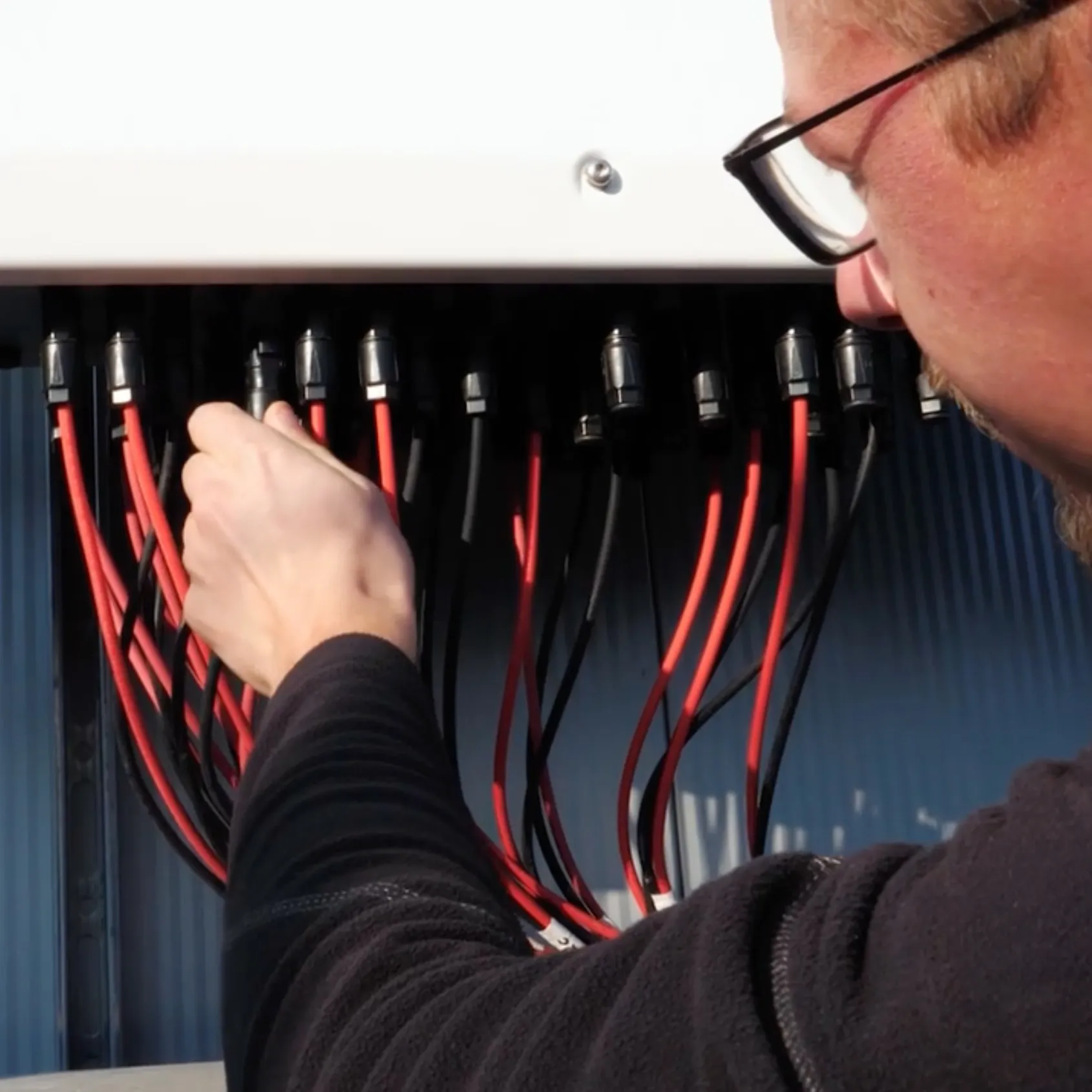 ESG-Mitarbeiter prüft rot-schwarze Kabel an einer elektrischen Anschlussleiste im Freien.