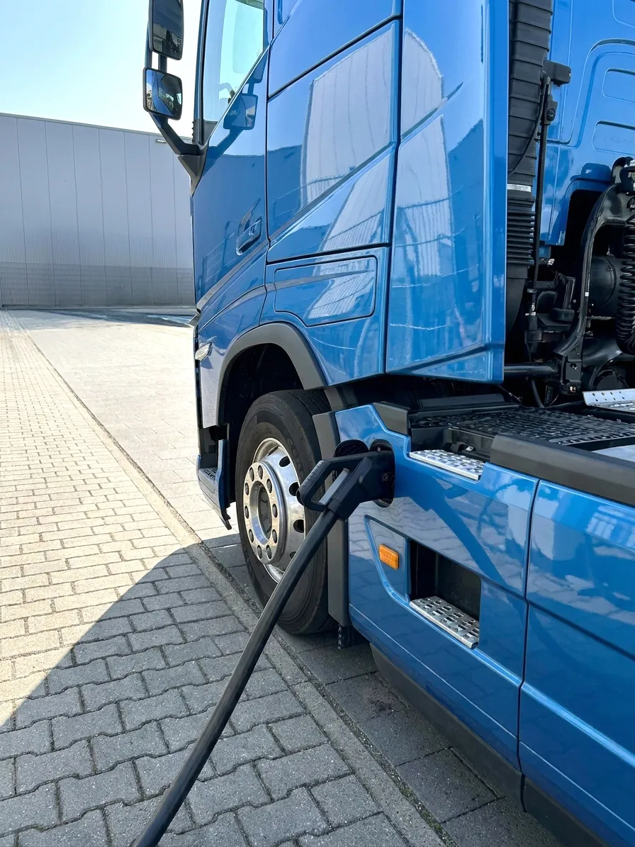 Blauer Lkw, der an einer ESG Ladestation mit schwarzem Ladekabel aufgeladen wird.