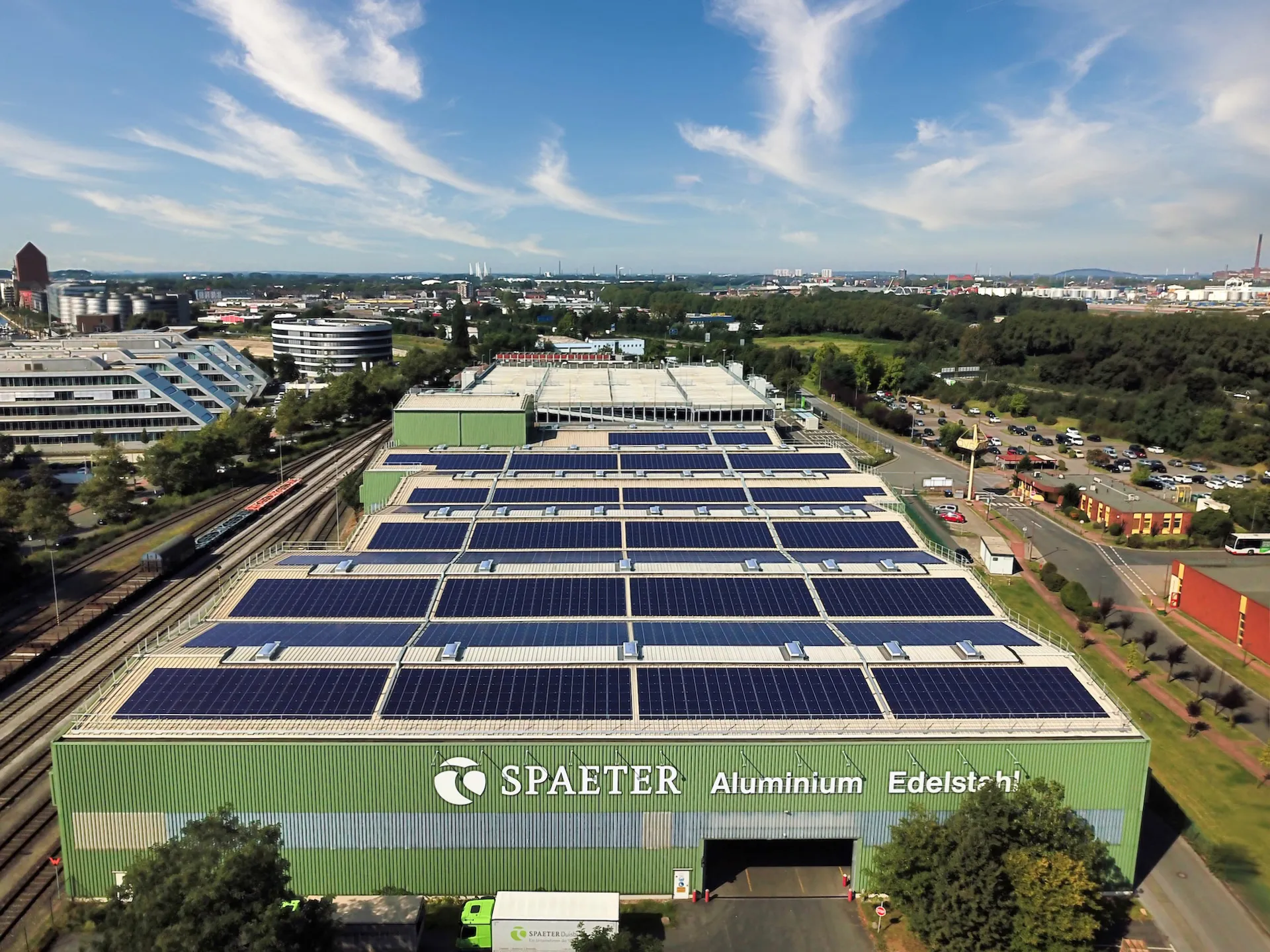 Große Fabrikhalle mit ESG Solarpaneelen auf dem Dach in einem Industriegebiet unter blauem Himmel.