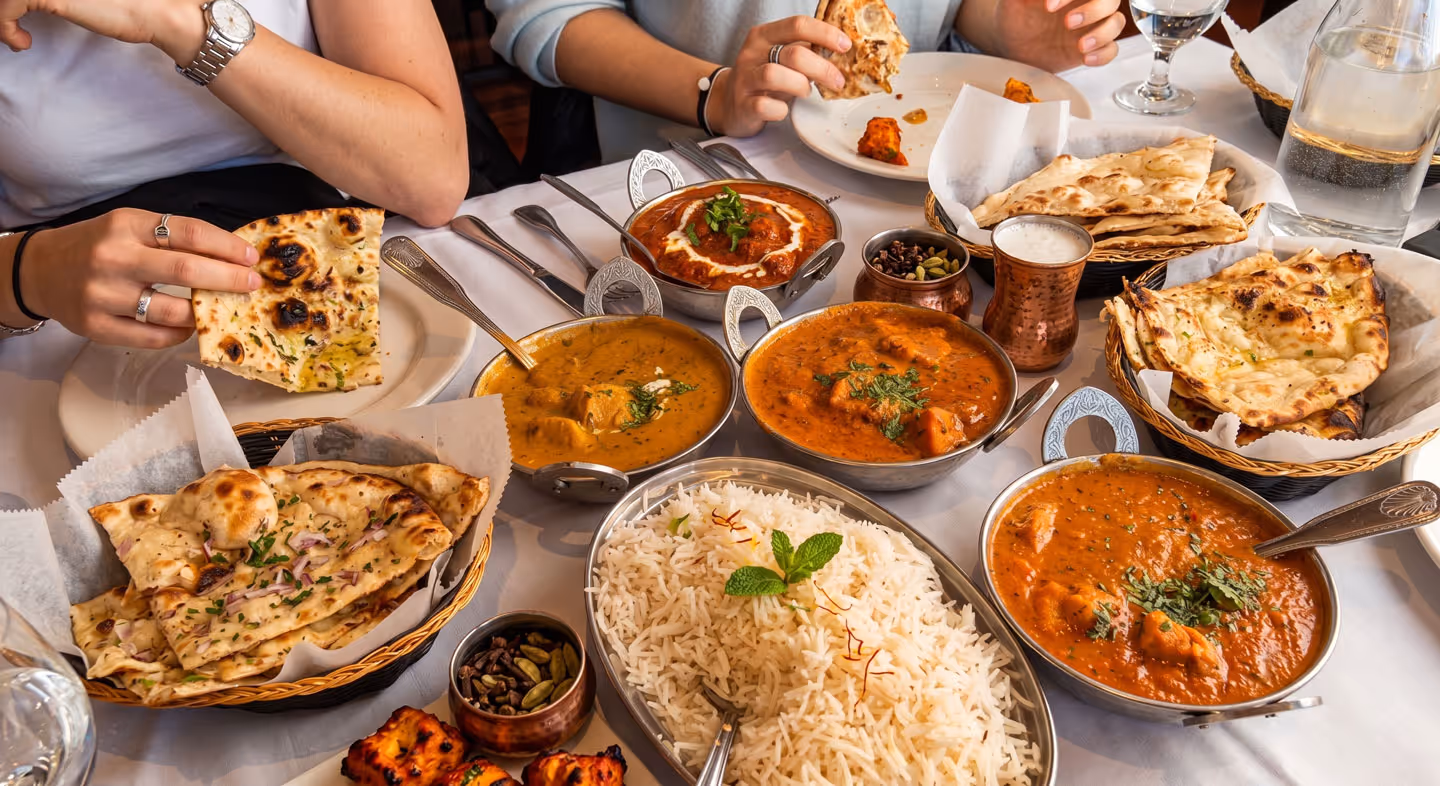Indian meal with naan, basmati rice, curry dishes, tandoori chicken, and two people eating at a table.