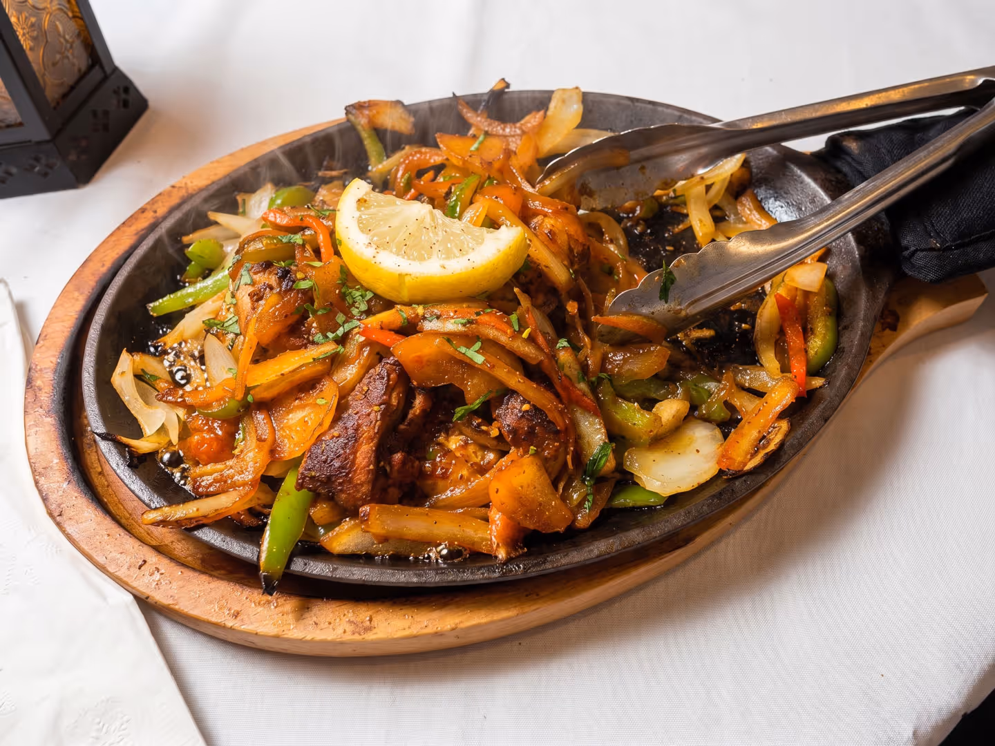 Sizzling plate of cooked chicken fajitas with grilled onions, peppers, and a lemon wedge on top.
