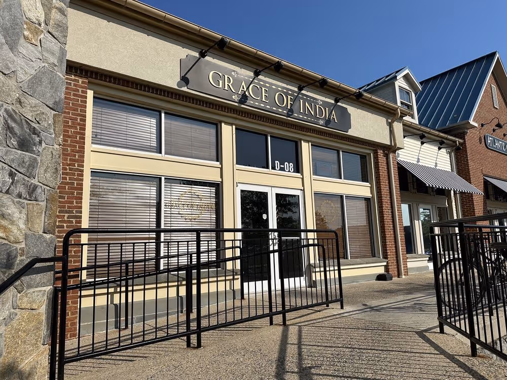 Storefront of Grace of India restaurant with large windows and entrance door under a sunny sky.