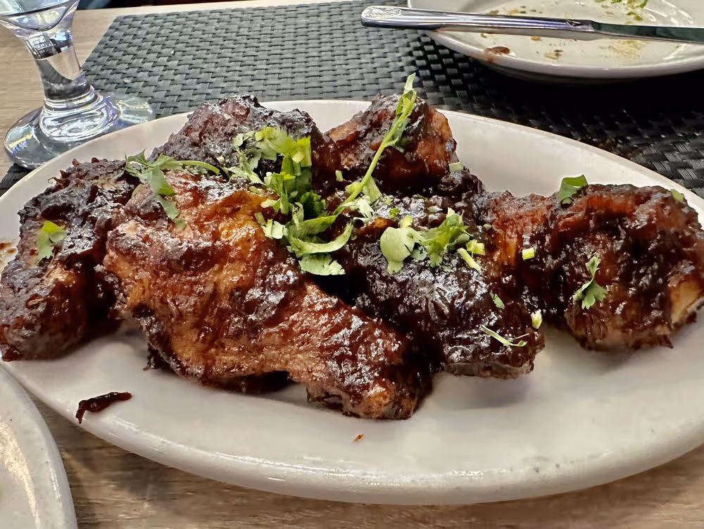 Plate of glazed barbeque ribs garnished with fresh chopped cilantro on a wooden table.
