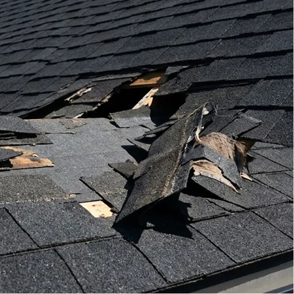 Asphalt shingle roof with significant damage, missing and broken shingles, and exposed wood underneath.