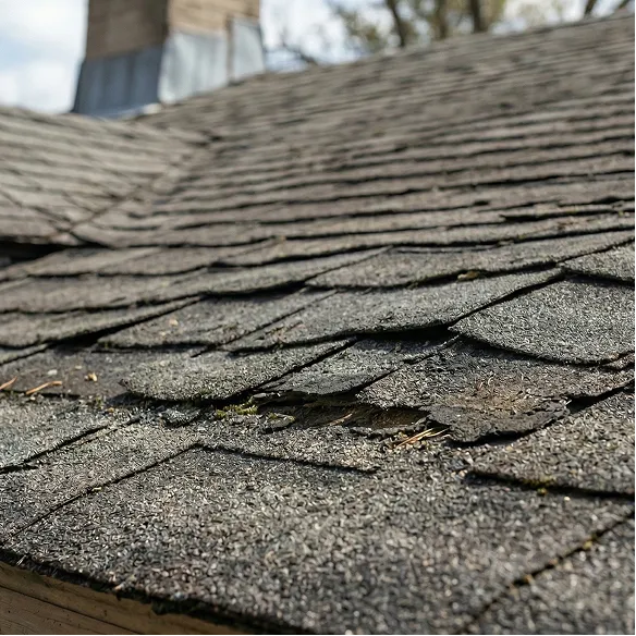 Close-up of an asphalt shingle roof with visible damage and curling shingles, indicating wear and need for repair.