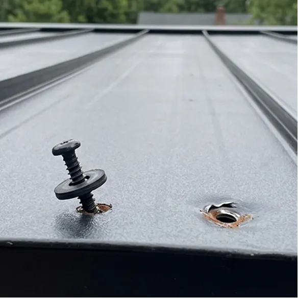 A loose screw is partially removed from a metal roof panel, next to a damaged and rust-stained screw hole.