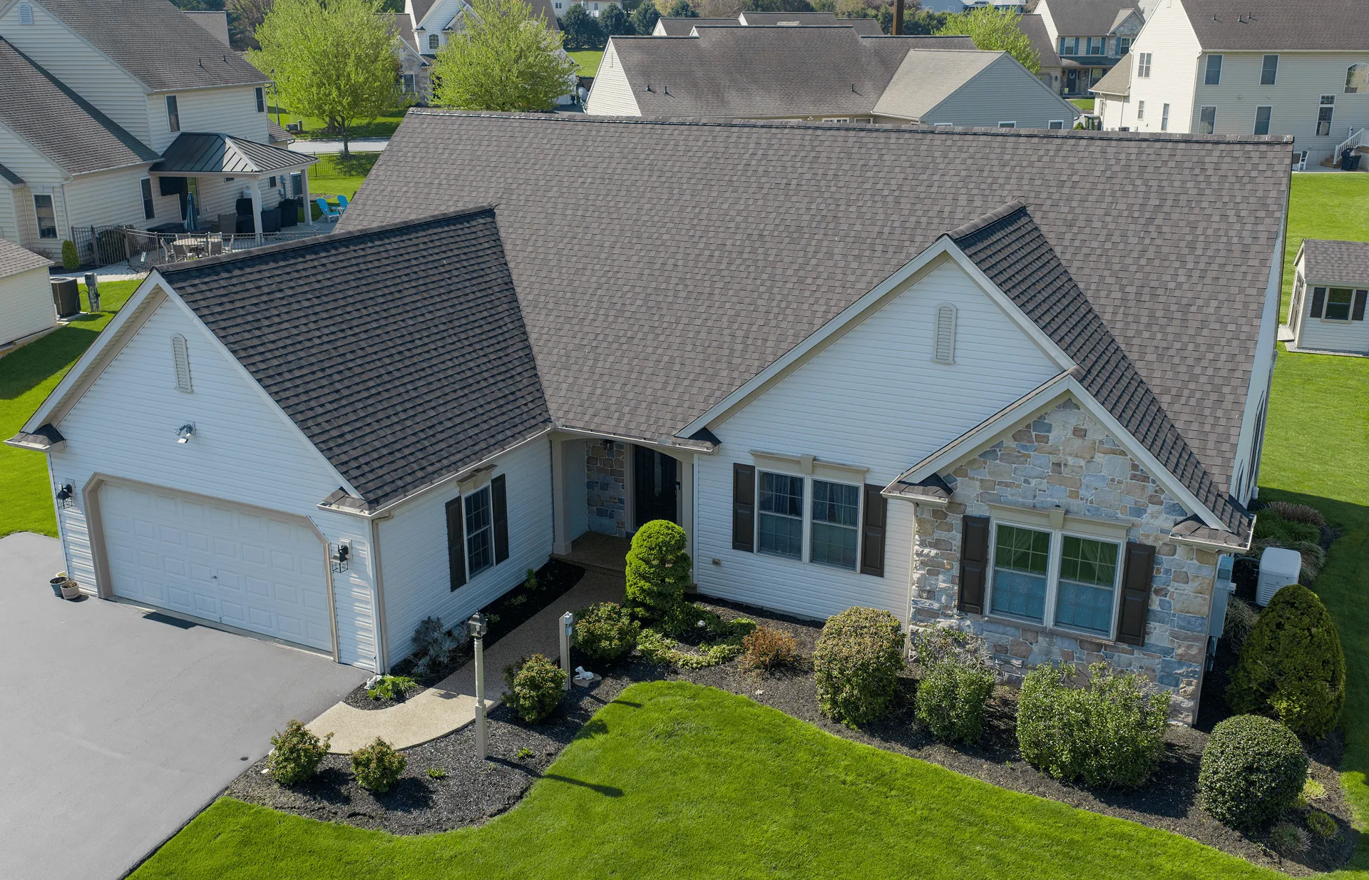 Single-story suburban house with a stone and vinyl exterior, attached two-car garage, manicured lawn, and landscaped front yard.