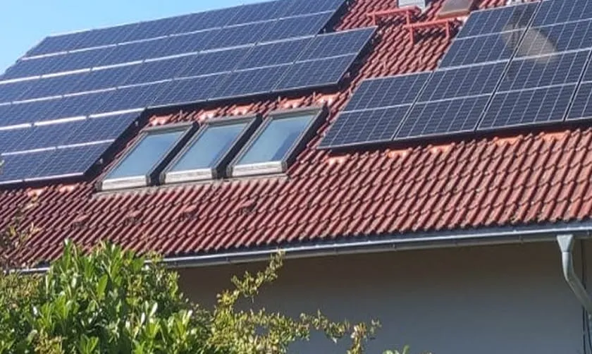 Ein rotes Ziegeldach mit zahlreichen Solarmodulen und drei Oberlichtern über dem Grün.