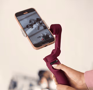 Person holding a purple smartphone gimbal stabilizer with a phone screen showing a grayscale photo being taken.