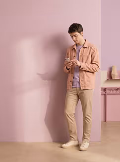 Young man in casual clothes standing indoors looking at his phone.