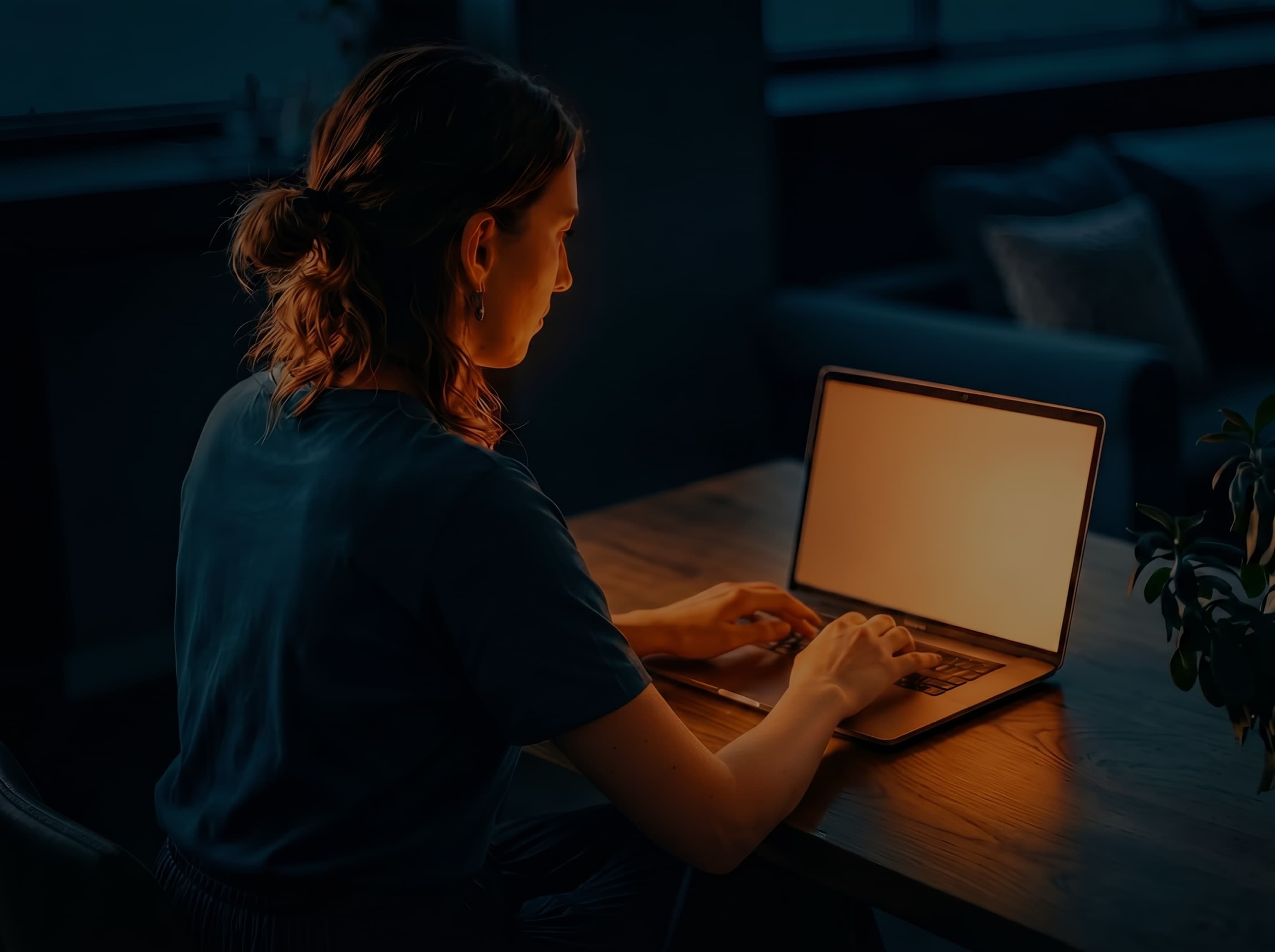 A designer working at a laptop by lamplight at a wooden table