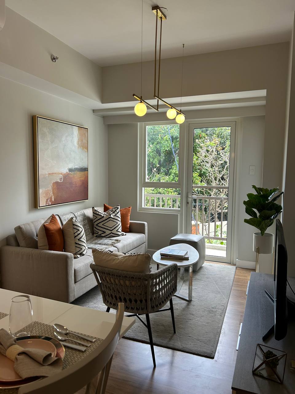 Living room with beige sofa, patterned pillows, a round table, armchair, and glass door leading outside.