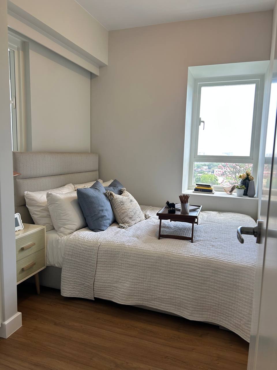 Minimalist bedroom with a bed, neutral bedding, pillows, bedside table, and window with city view.