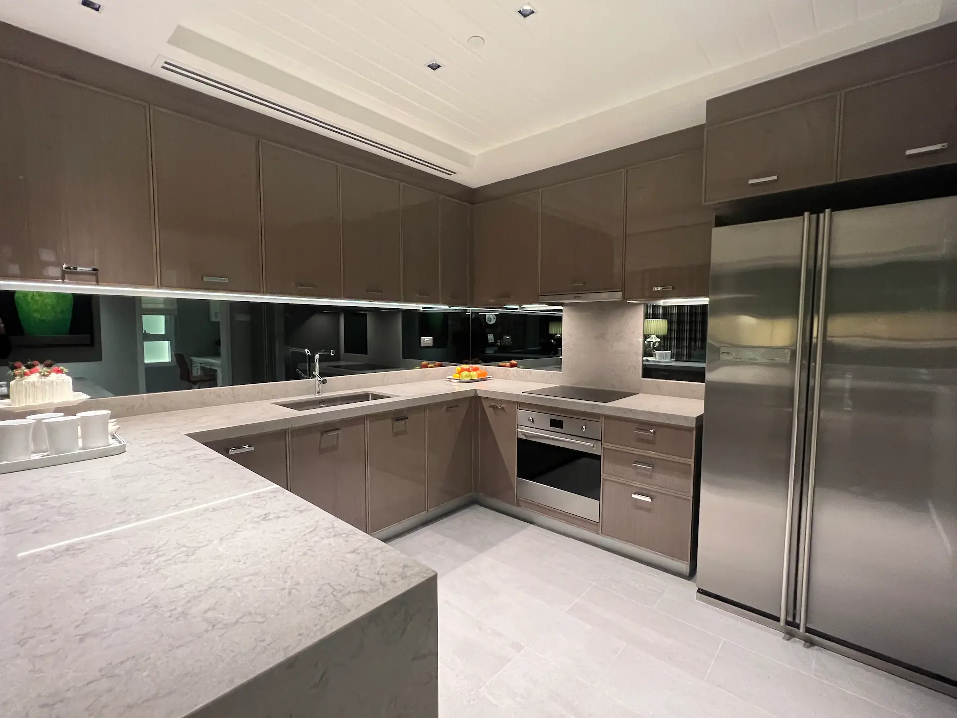 Modern kitchen with beige cabinetry, marble countertops, built-in oven, and stainless steel fridge.