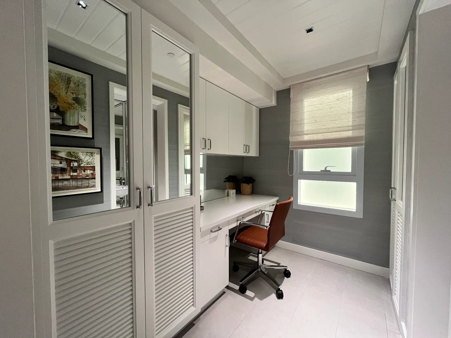 Small home office with white built-in cabinets and a brown rolling desk chair by a window with shade.
