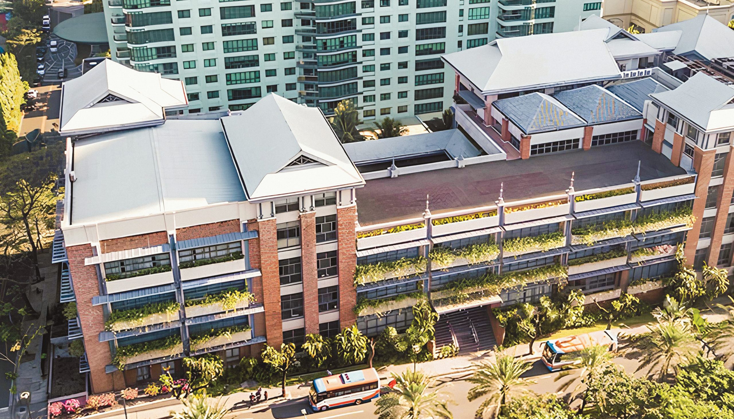 Aerial view of a modern multi-story building with balconies covered in plants and buses on the street below.