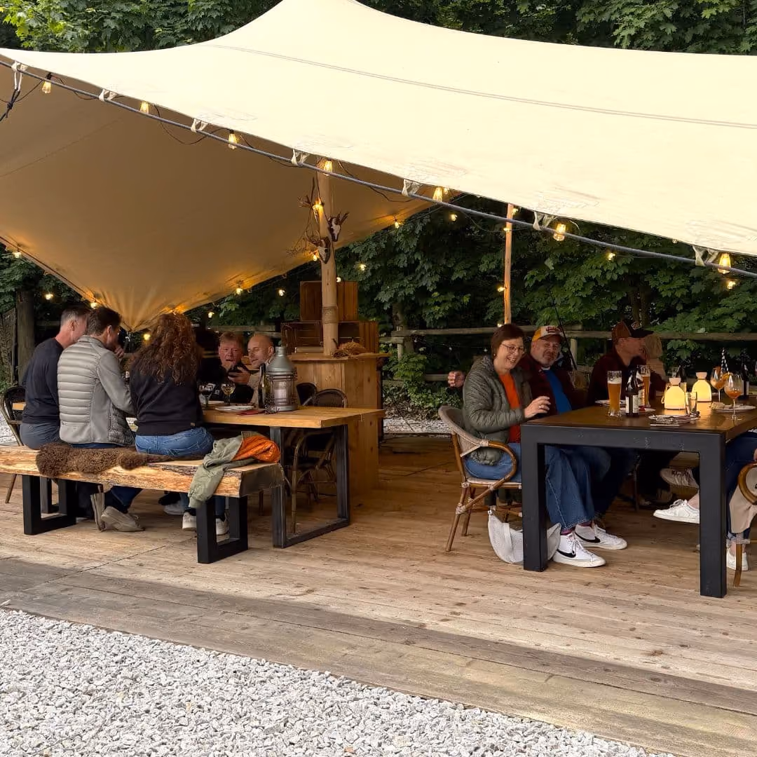 Gäste sitzen an langen Tischen unter der überdachten Zeltküche bei einem Outdoor-Cooking-Abend im Harz Hotel Iris