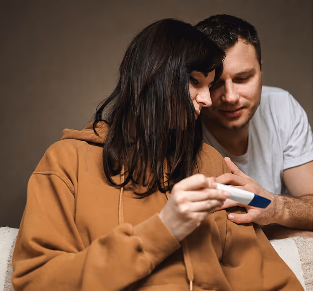 Couple looking at a pregnancy test with hopeful expressions while sitting indoors.