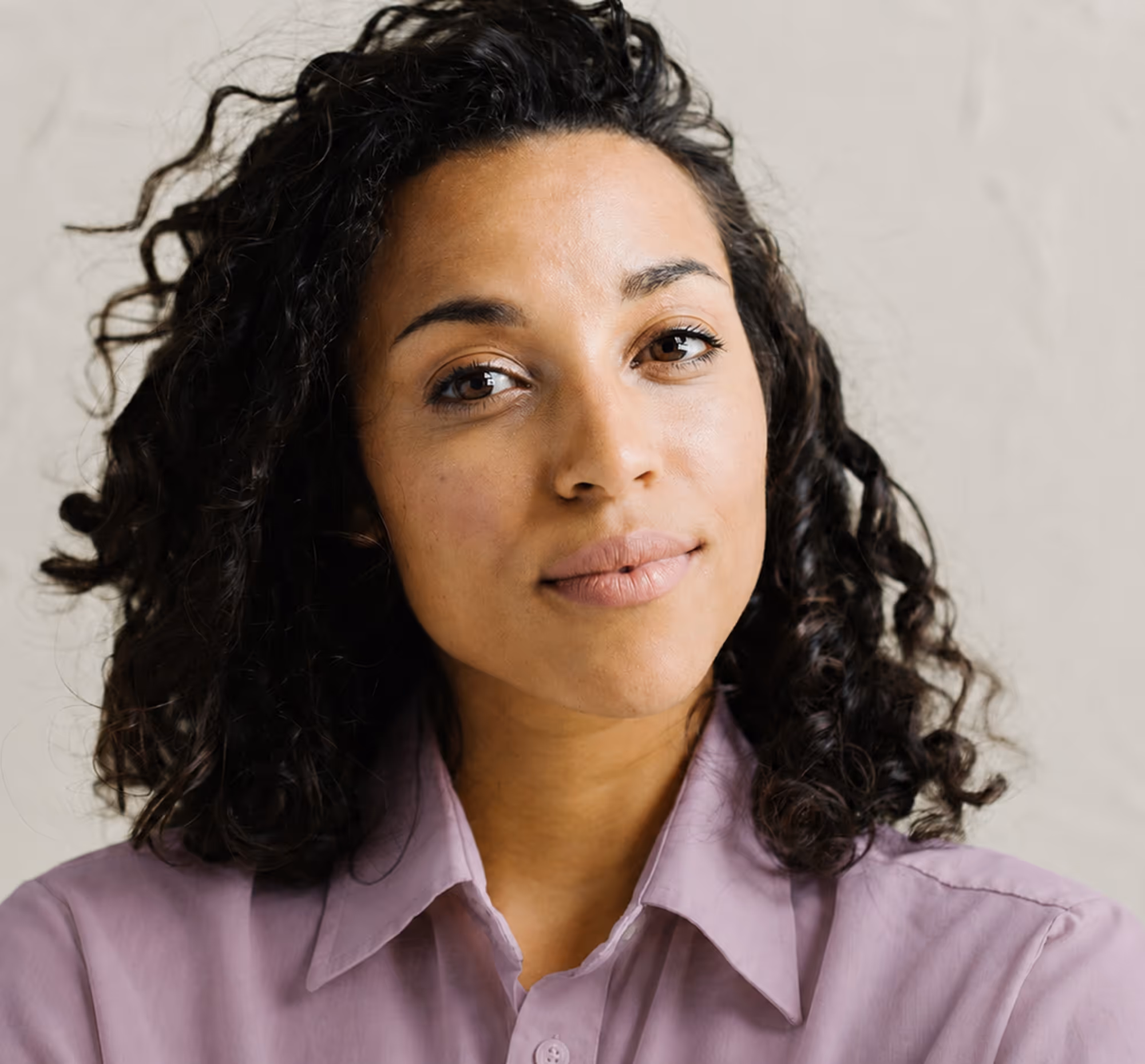 Confident woman with curly dark hair wearing a light purple button-up shirt.