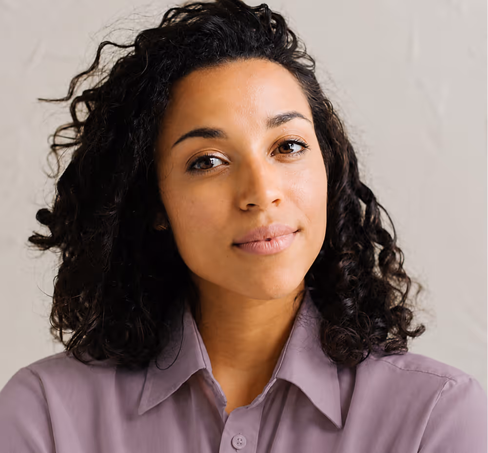 Confident woman with curly dark hair wearing a light purple button-up shirt.