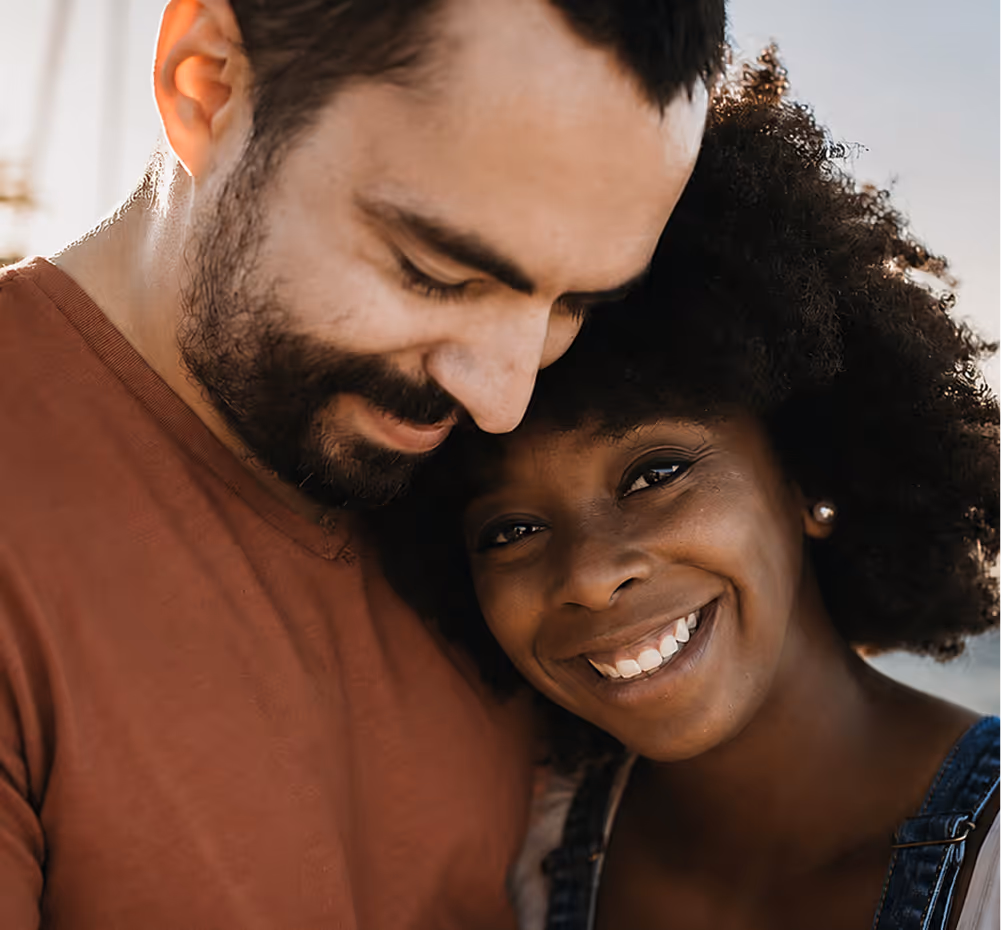 Smiling young woman with afro leaning on a man in a rust shirt in an outdoor setting.