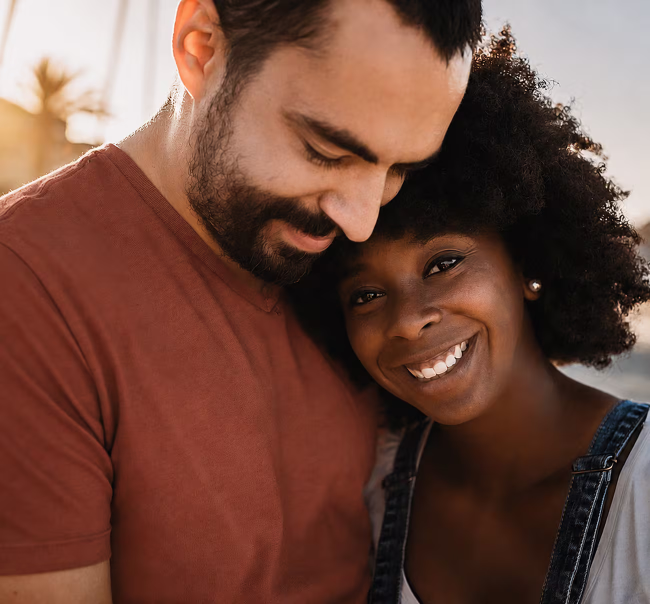 Smiling young woman with afro leaning on a man in a rust shirt in an outdoor setting.
