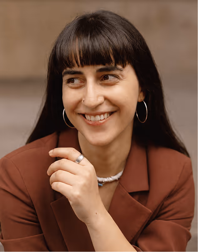 Smiling woman with dark hair, hoop earrings, and brown blazer looking to the side.