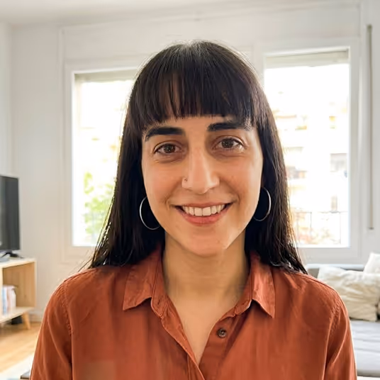 Smiling woman with straight black hair and bangs wearing a rust-colored shirt indoors.