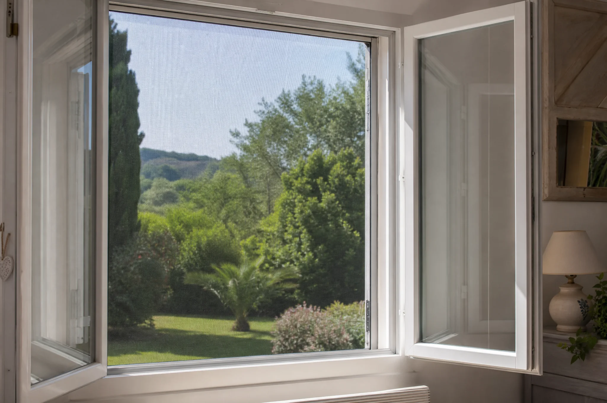 Fenêtre ouverte équipée d'une moustiquaire avec vue sur le jardin