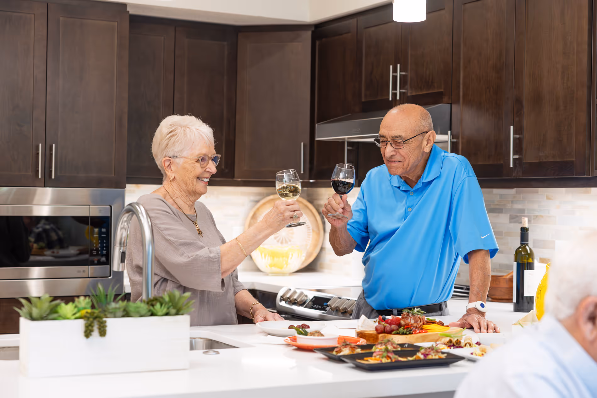 Senior residents enjoying a meal and conversation in a modern kitchen, raising glasses during a social gathering in a bright retirement community home.