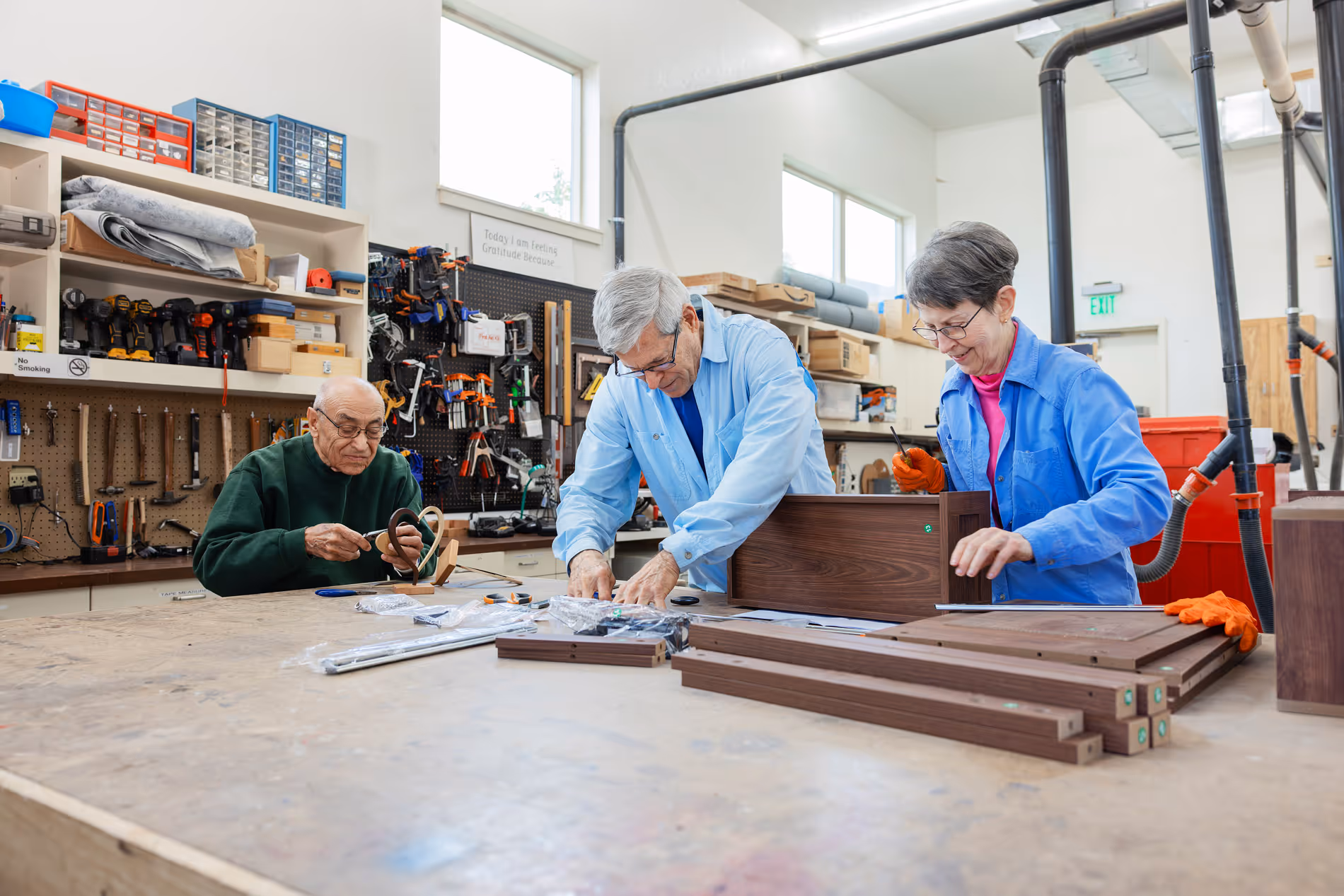 Three seniors working on woodworking projects in a bright, well-equipped workshop.