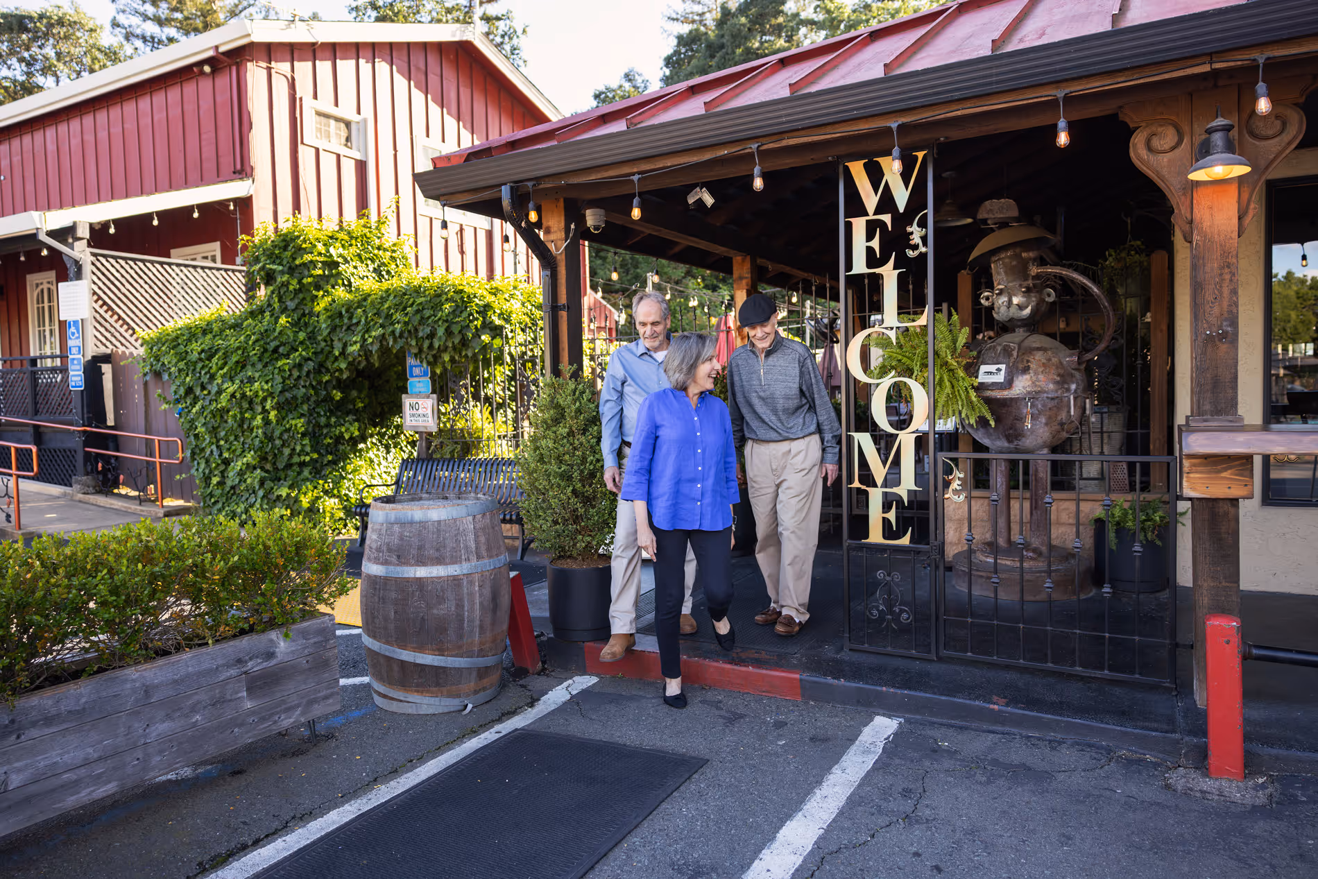 Three elderly people happily leaving a rustic restaurant with a vertical welcome sign.