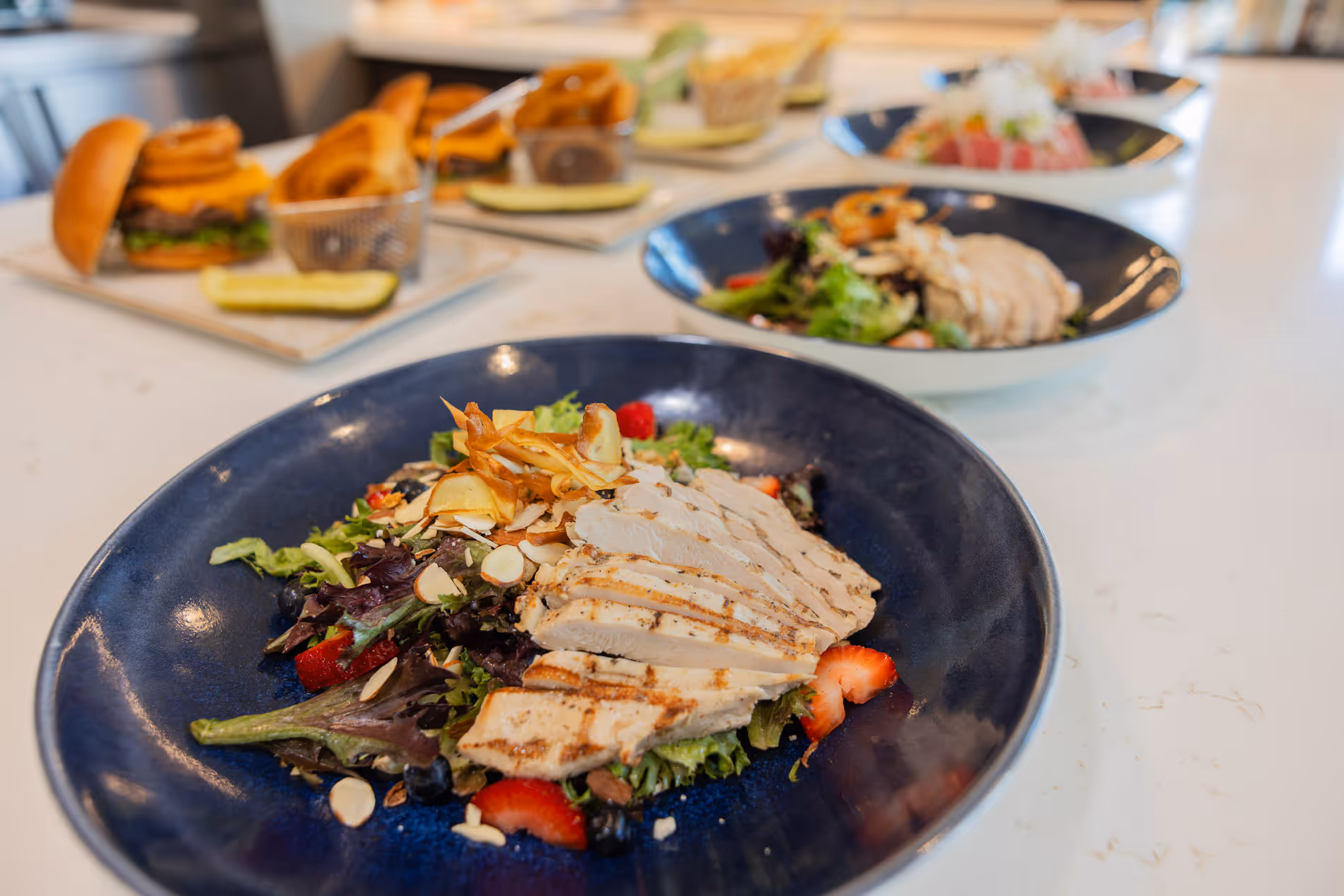 Plates of grilled chicken salad with strawberries and almond slices on a table.