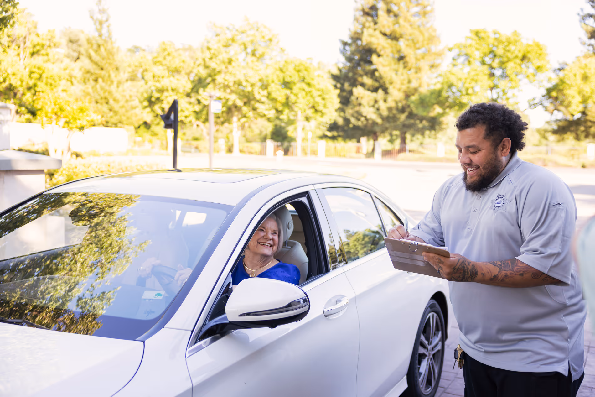 A woman in a car smiles at a man holding a clipboard outside the vehicle.