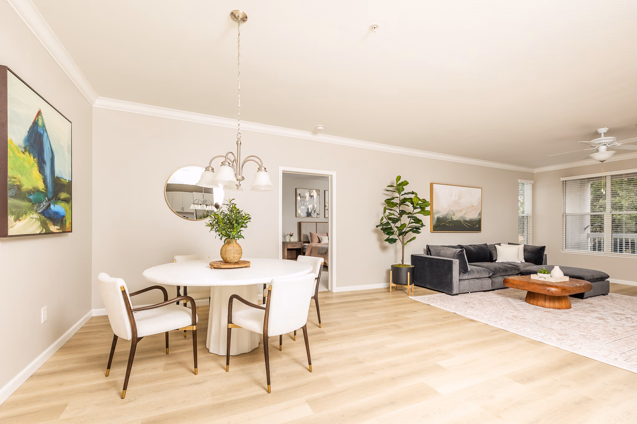 A bright living room with a round dining table, chairs, gray couch, and wall art.